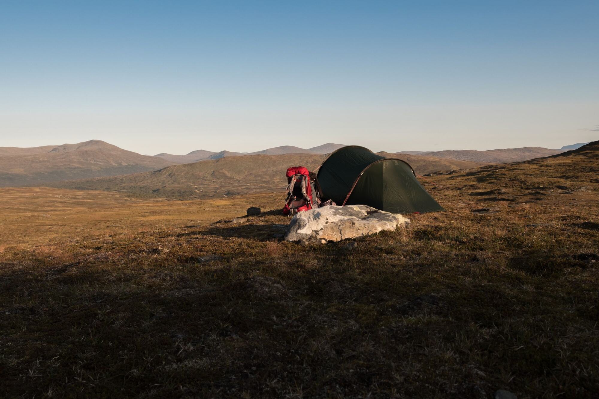 Une tente et un sac à dos dans la montagne, au soleil couchant